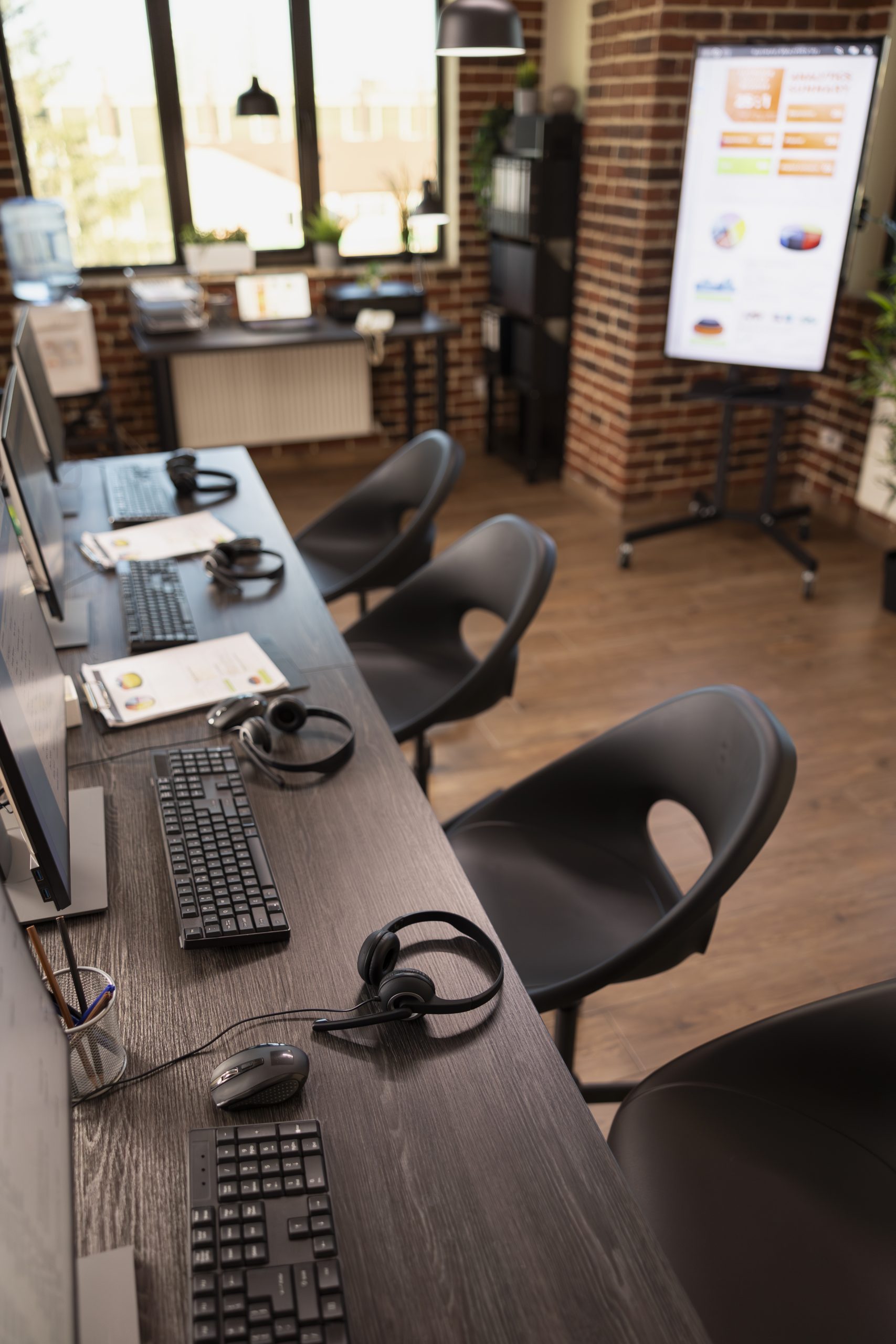Modern office with nobody present is organized with computer systems and multiple chairs. A well arranged brick wall workplace, ready for company analysis and marketing discussions among employees.